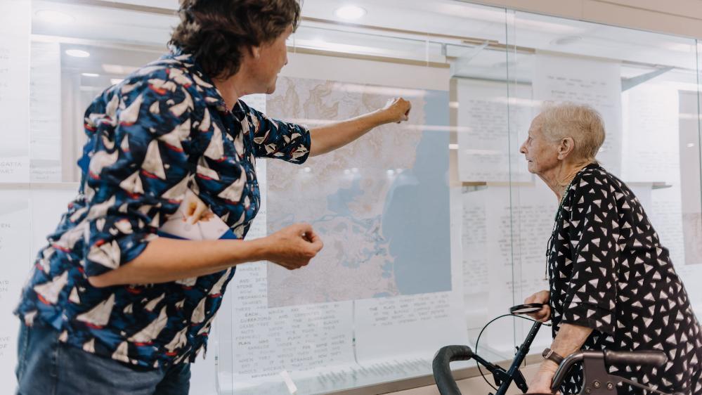 Dr Jen Saunders points to a map as part of her art exhibition. She is with a lady who is using a walker. Photo: Michael Gray