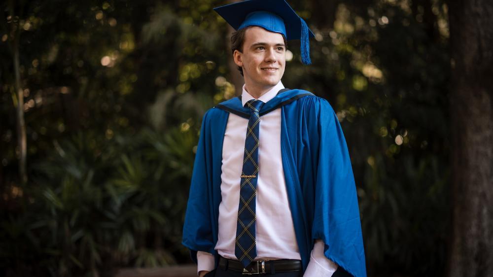 Jackson Cocks stands in a blue graduation gown and cap. Photo: Michael Gray