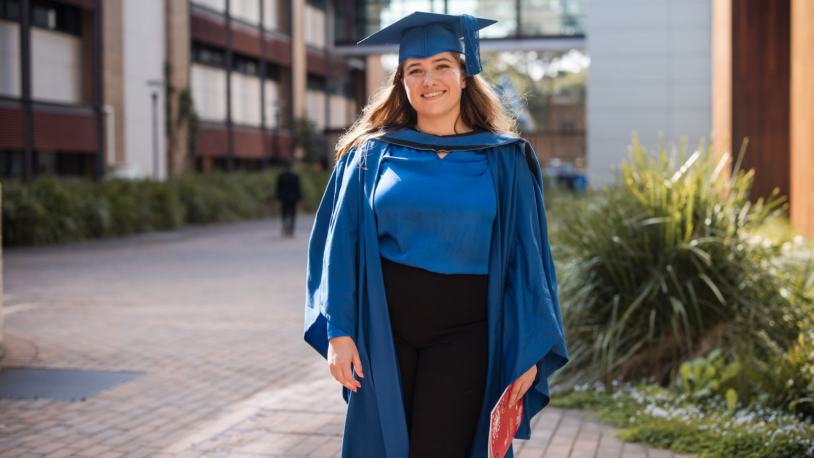 Emma Newman in a blue graduation gown in a full length image. Photo: Michael Gray