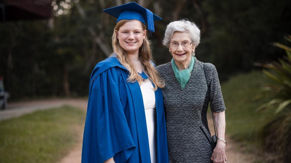 Elizabeth Caine has a smile on her face and wears a graduation gown and cap. She stands next to her grandmother Judith. Photo: Michael Gray