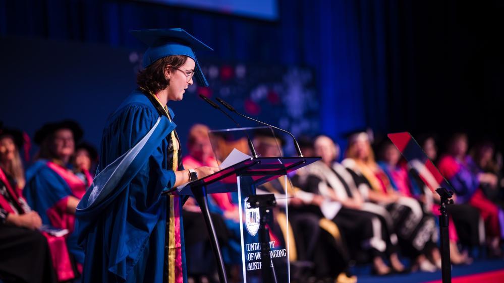 Caitlin Liddle stands on stage at graduation and delivers a speech to the audience. Photo: Michael Gray