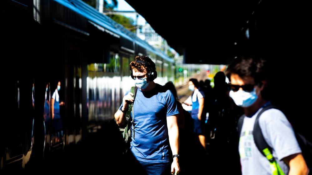 Students wait for a train, wearing masks. Photo: Paul Jones