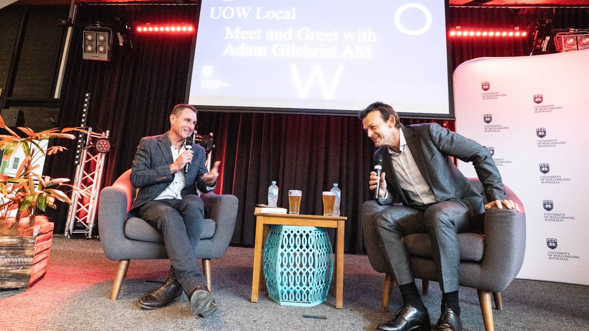 Jeremy Wilshire and Adam Gilchrist chat on stage as they sit in armchairs during the UOW Local event at UniBar. Photo: Paul Jones