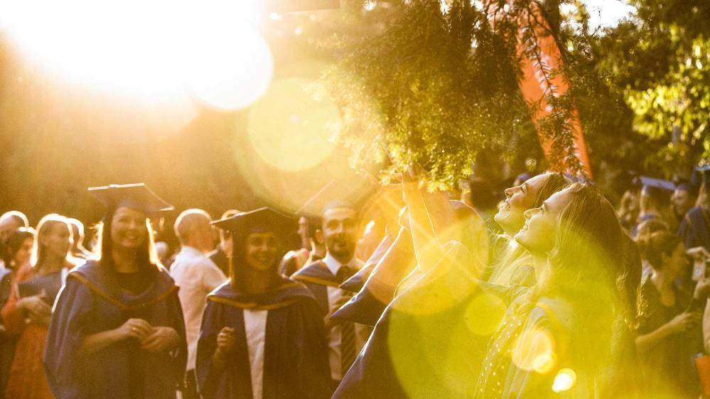 A group of students celebrate their graduations by throwing their blue hats into the air. Photo: Paul Jones