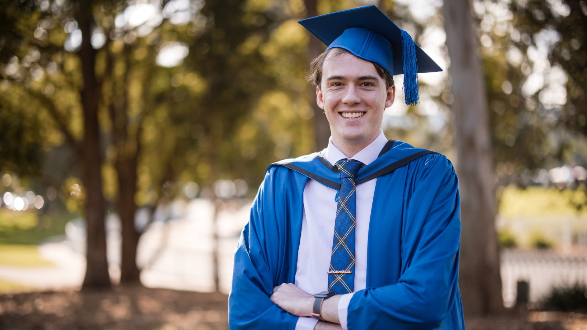 Jackson Cocks stands with his hands crossed in a blue graduation gown and cap. Photo: Michael Gray