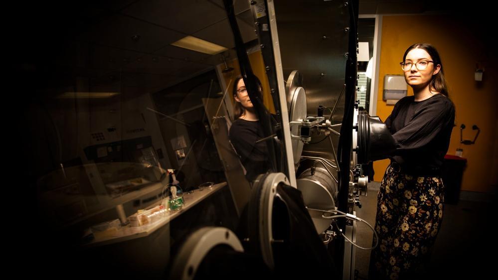 Dr Jessie Posar uses a machine in a physics laboratory at UOW. Her hands are in a machine and her face is reflected in the machine. Photo: Paul Jones