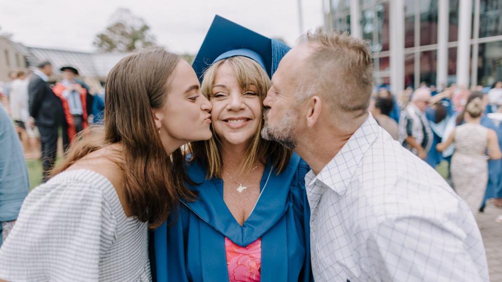 Juliet Carter, centre with a graduation gown and cap, is kissed on the cheek by her daughter (left) and husband (right). Photo: Michael Gray