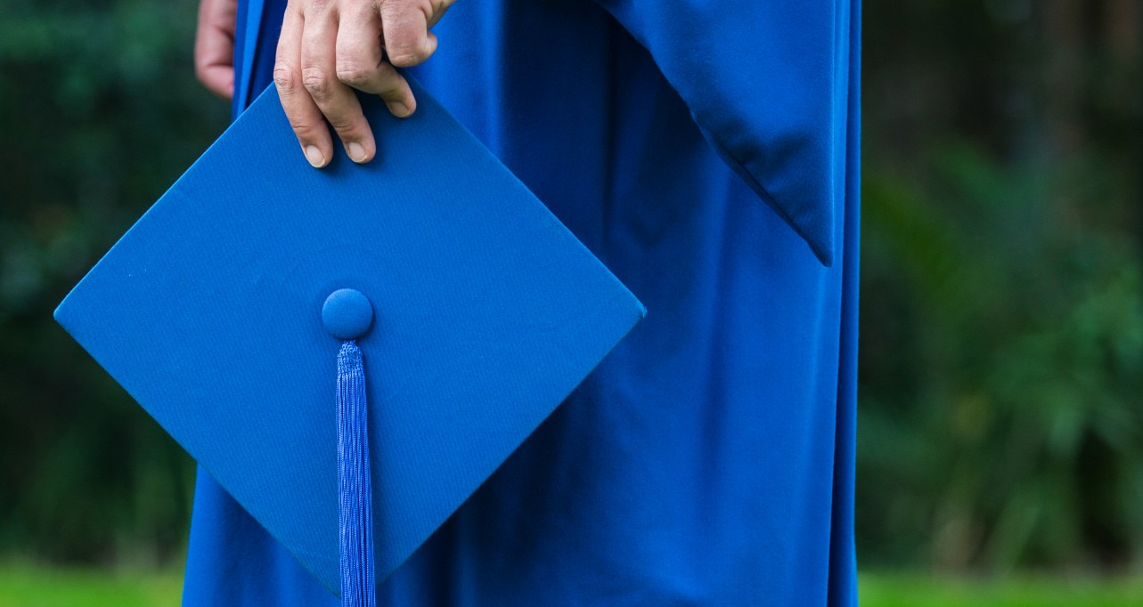 An image of a man holding a blue mortar graduation. The close up is on the hat. Photo: Paul Jones