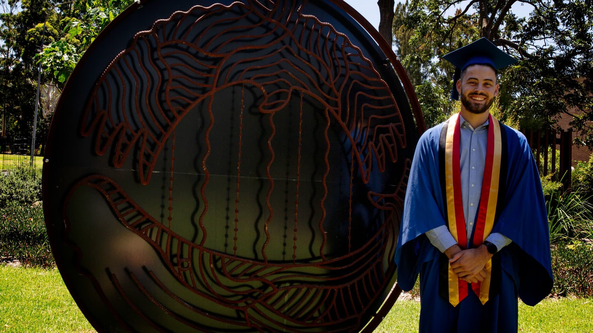 UOW graduate Mitchell Strange stands in front of the sign for Woolyungah Indigenous Centre.