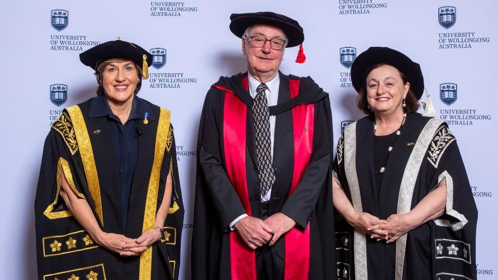 Chancellor Christine McLoughlin, Professor Nicholas Dixon and Vice-Chancellor Professor Patricia M Davidson stand in front of a UOW media wall wearing graduation gowns. Photo: Andy Zakeli