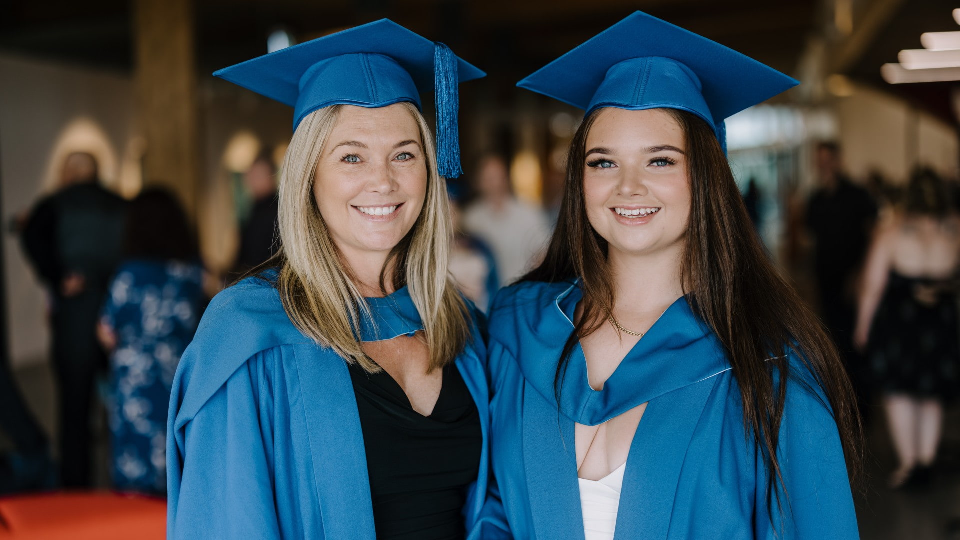 Nicole and Holli Pritchard, wearing blue graduation gowns and caps, stand next to each other and smile. Photo: Michael Gray