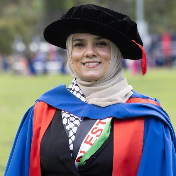 Dr Noor Jarbou wears a black graduation cap and blue and red gown. She smiles at the camera. Photo: Mark Newsham