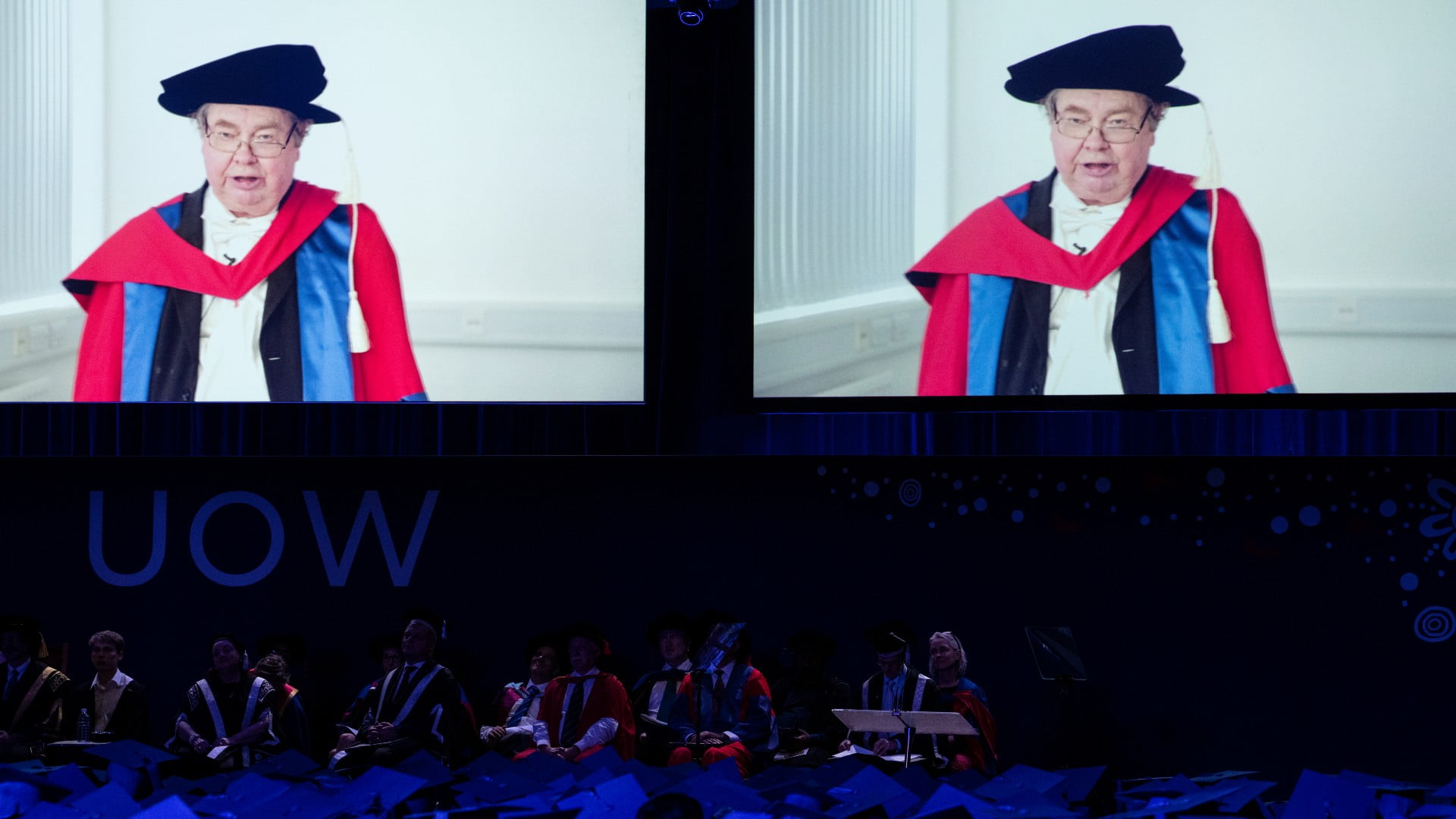 Professor Robin Thompson, pictured on a video screen in a graduation gown and cap, speaks to the audience at the UOW graduation ceremony. Photo: Paul Jones