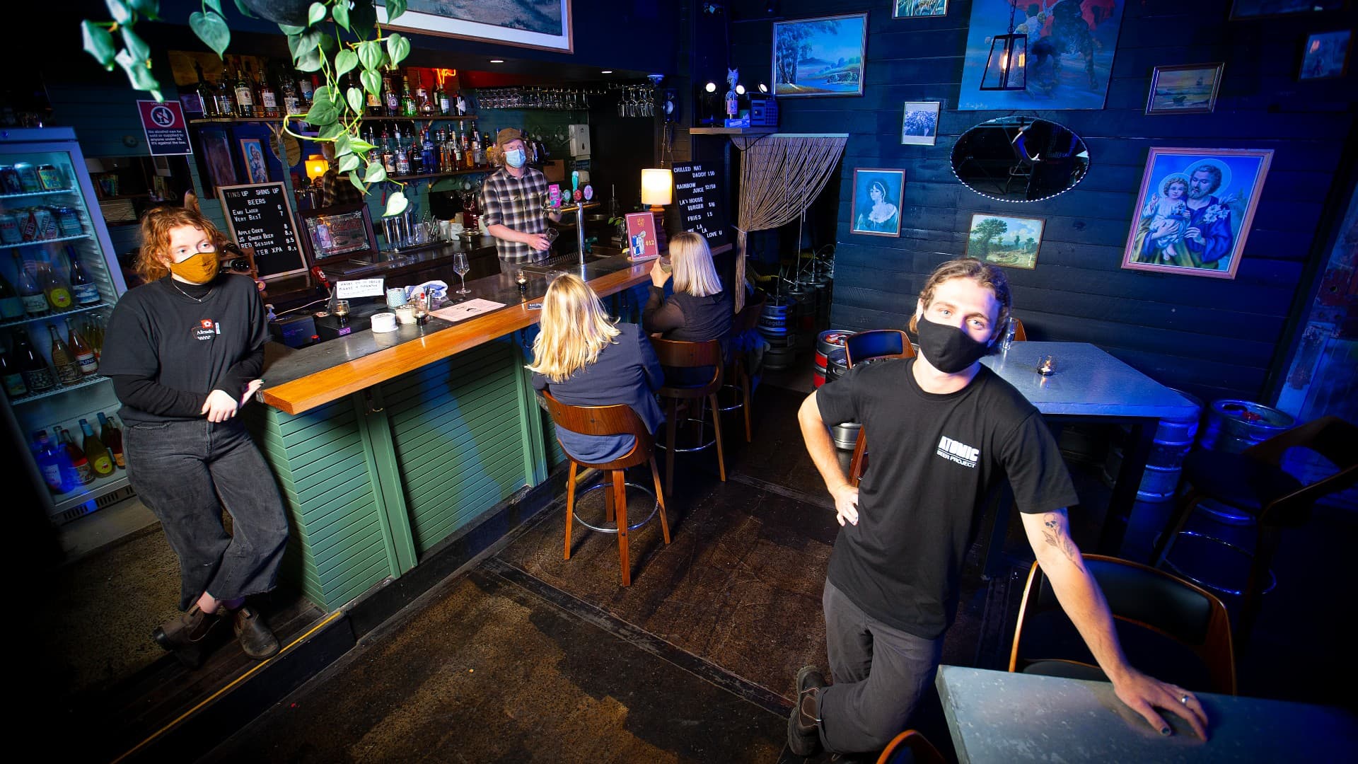 Three bartenders are pictured standing in a bar in Wollongong, with two patrons on stools. Photo: Paul Jones
