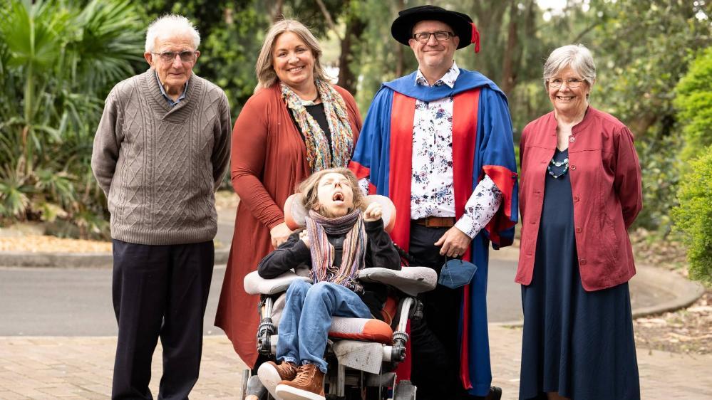 Dr Shawn Burns with his family on graduation day. From left, his father in law, his wife Gina, Shawn, and his mother. In front is his son Mack, who is in a wheelchair. They are all smiling at the camera. Photo: Paul Jones
