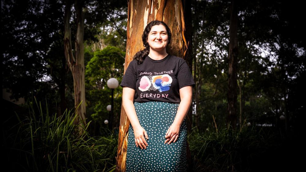 PhD Stephanie Beaupark, wearing a black shirt and green skirt, stands against a tree. Photo: Paul Jones