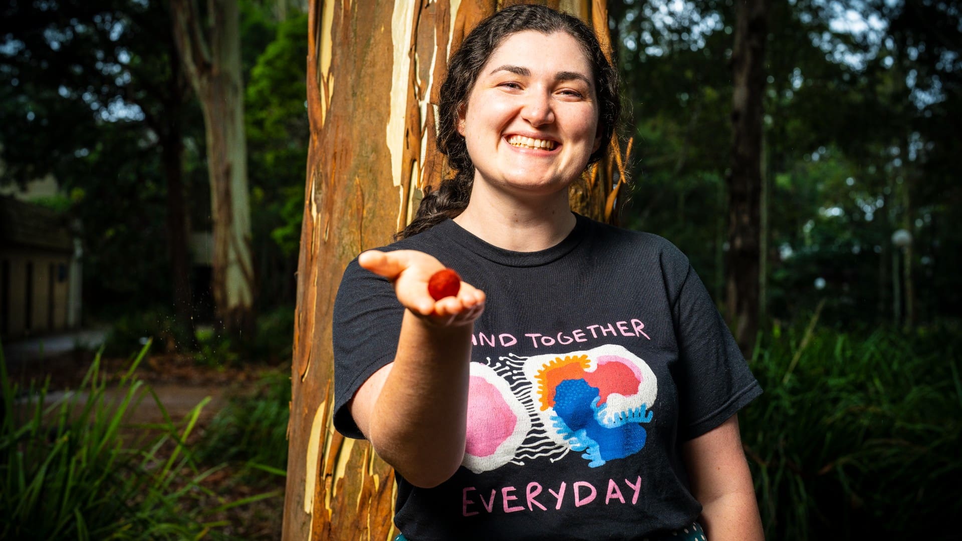 PhD Stephanie Beaupark, wearing a black shirt and green skirt, stands against a tree. She holds a handful of red berries towards the camera.  Photo: Paul Jones