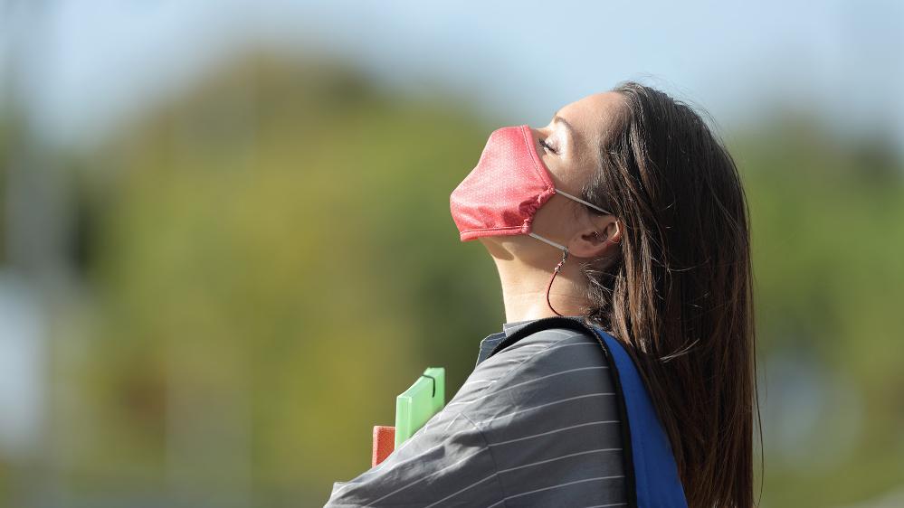 Young female student enjoys the sunshine wearing a mask