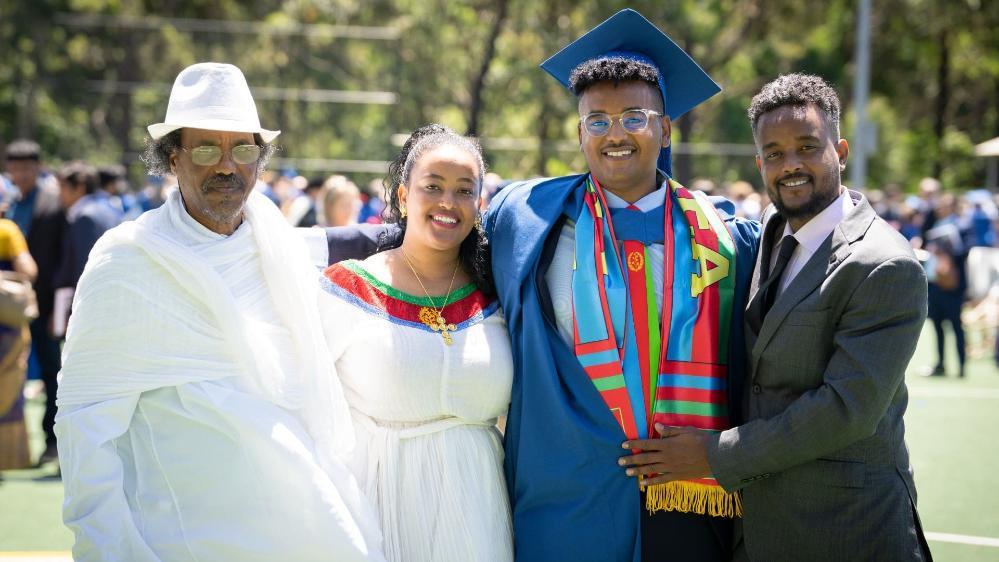 Teklemariam Mengistu, in a blue graduation gown, with (from left) his grandfather, wearing all white, his sister, wearing a white dress, and his brother, wearing a black suit. The whole family is smiling at the camera. Photo: Paul Jones