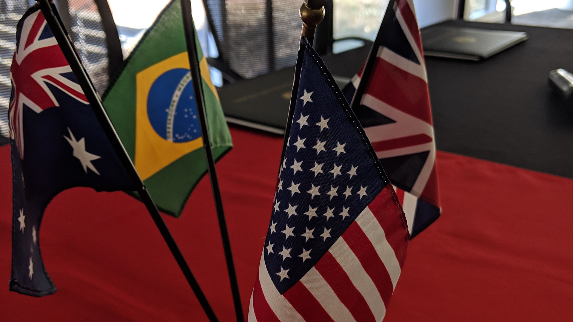 Image from 2019 UGPN conference of Australian, Brazilian, UK and USA flags on a deskflags