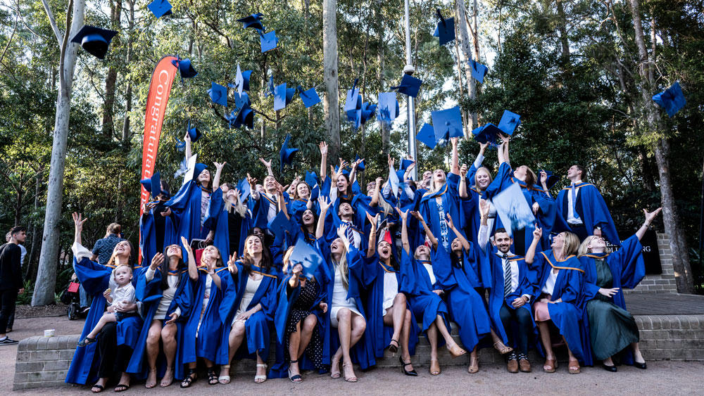 A group of students celebrate their graduations by throwing their blue hats into the air. Photo: Paul Jones