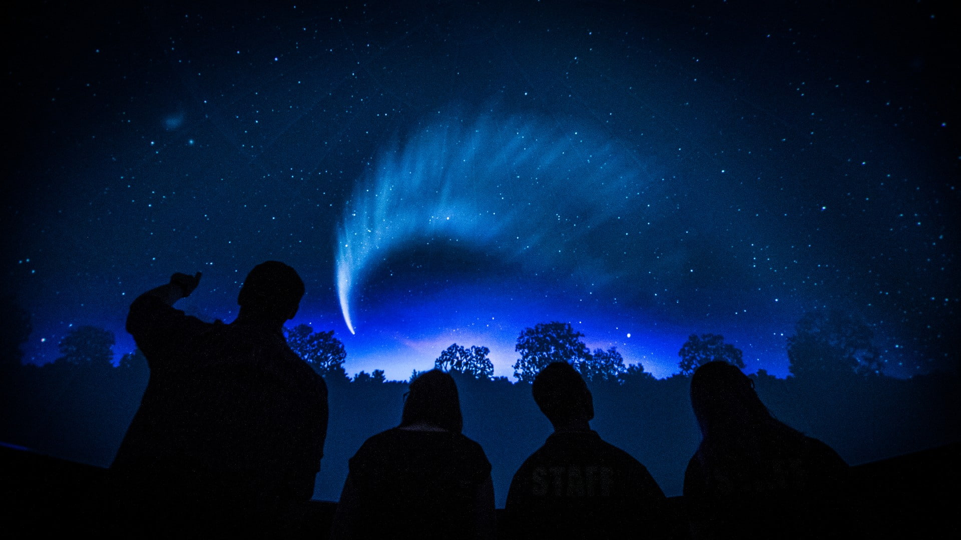 Four people are silhouetted against the backdrop of the Science Space planetarium. Photo: Paul Jones