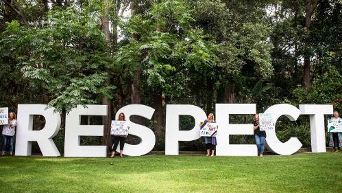 Members of the Safe and Respectful Communities team stand next to a large "Respect" sign