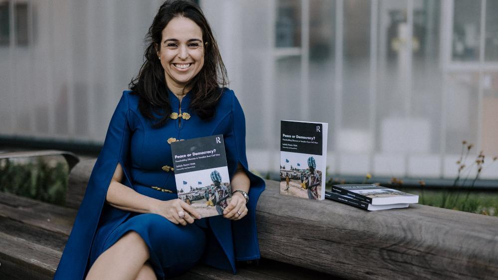 Izabela Pereira Watts sitting on a bench holds a copy of her new book. Photo: Michael Gray