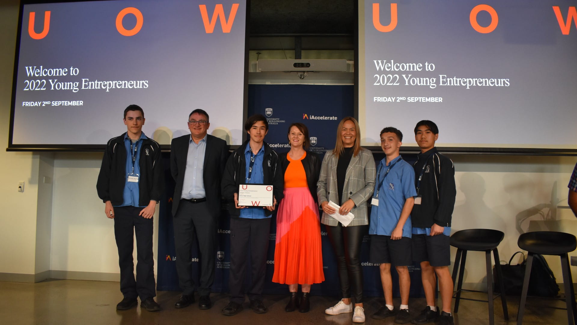 Students from Keira High School, wearing blue jumpers, stand in front of two UOW screens.