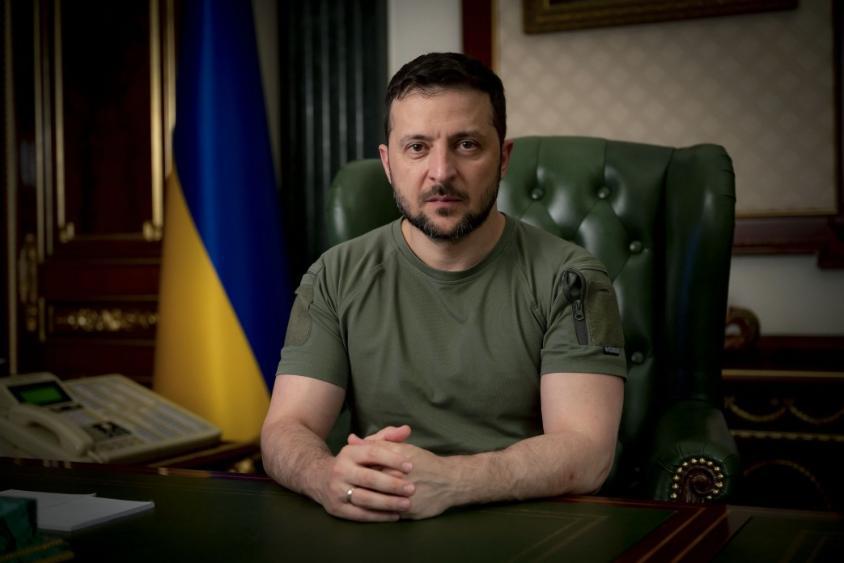 Ukrainian President Volodymyr Zelensky sits in a green chair, wearing a green shirt. The Ukranian flag is in the background. Photo: Submitted