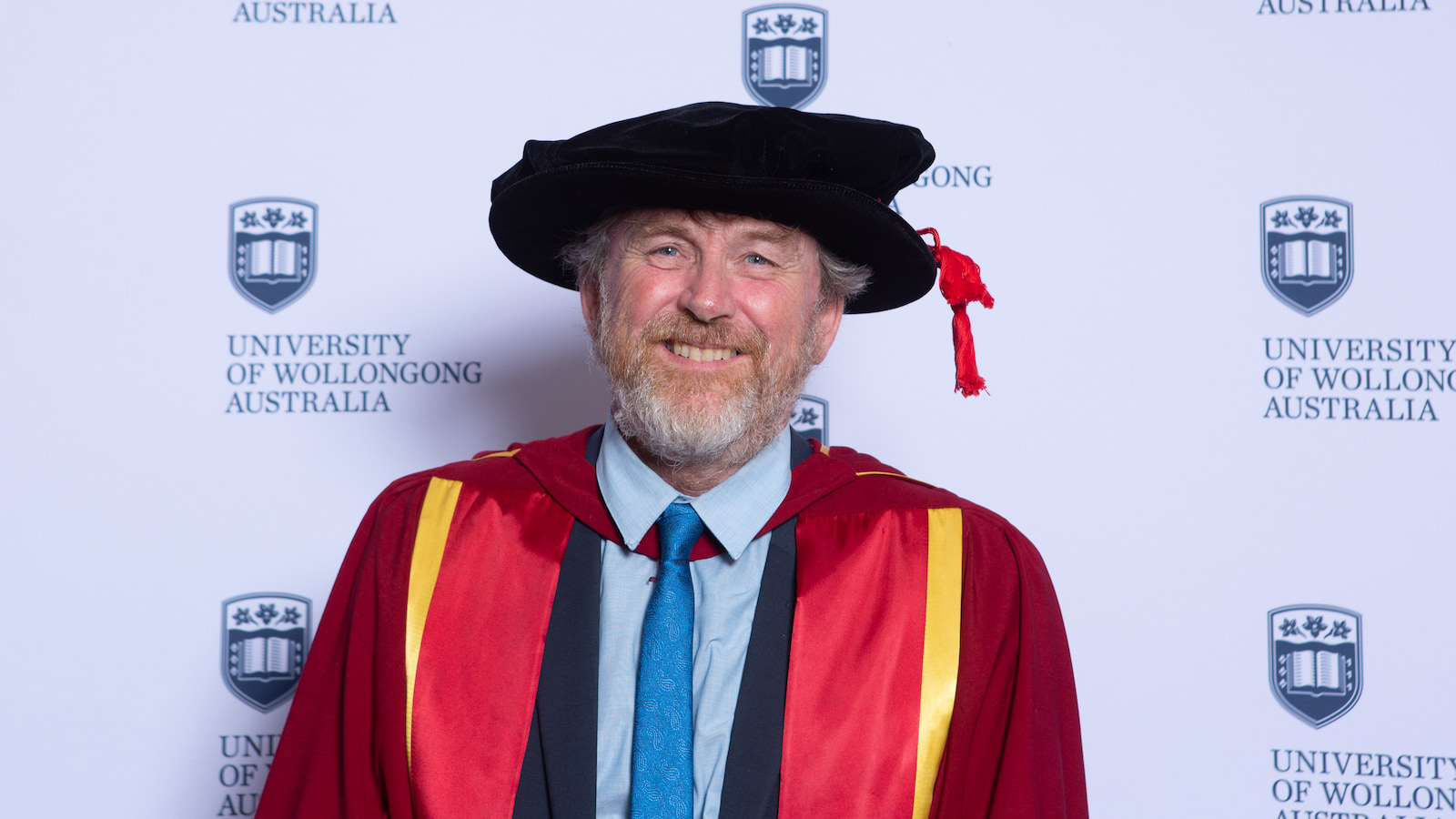 Professor Will Price, wearing a maroon graduation gown and black cap. Photo: Andy Zakeli
