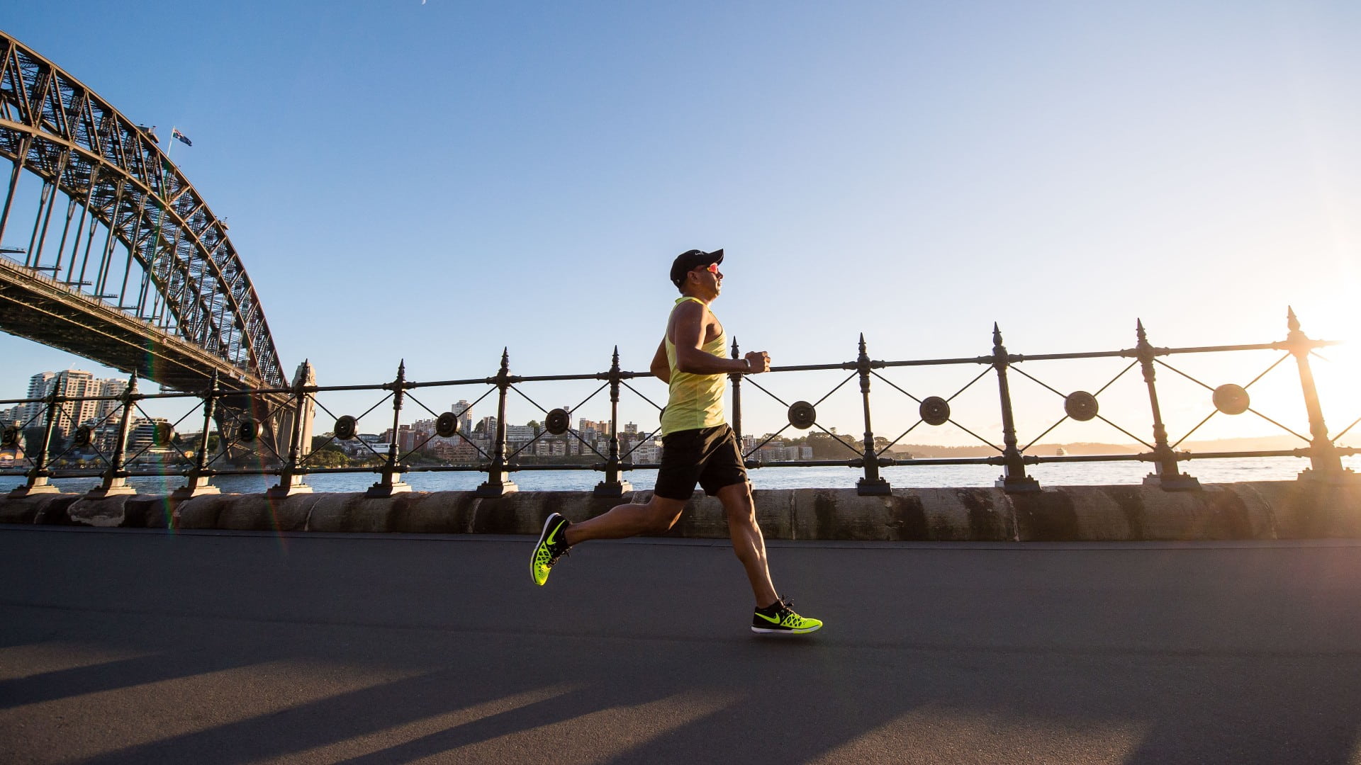 A man wearing fluro yellow sneakers and sunglasses runs along a road in Sydney, with the Harbour Bridge in the background. Photo: Unsplash