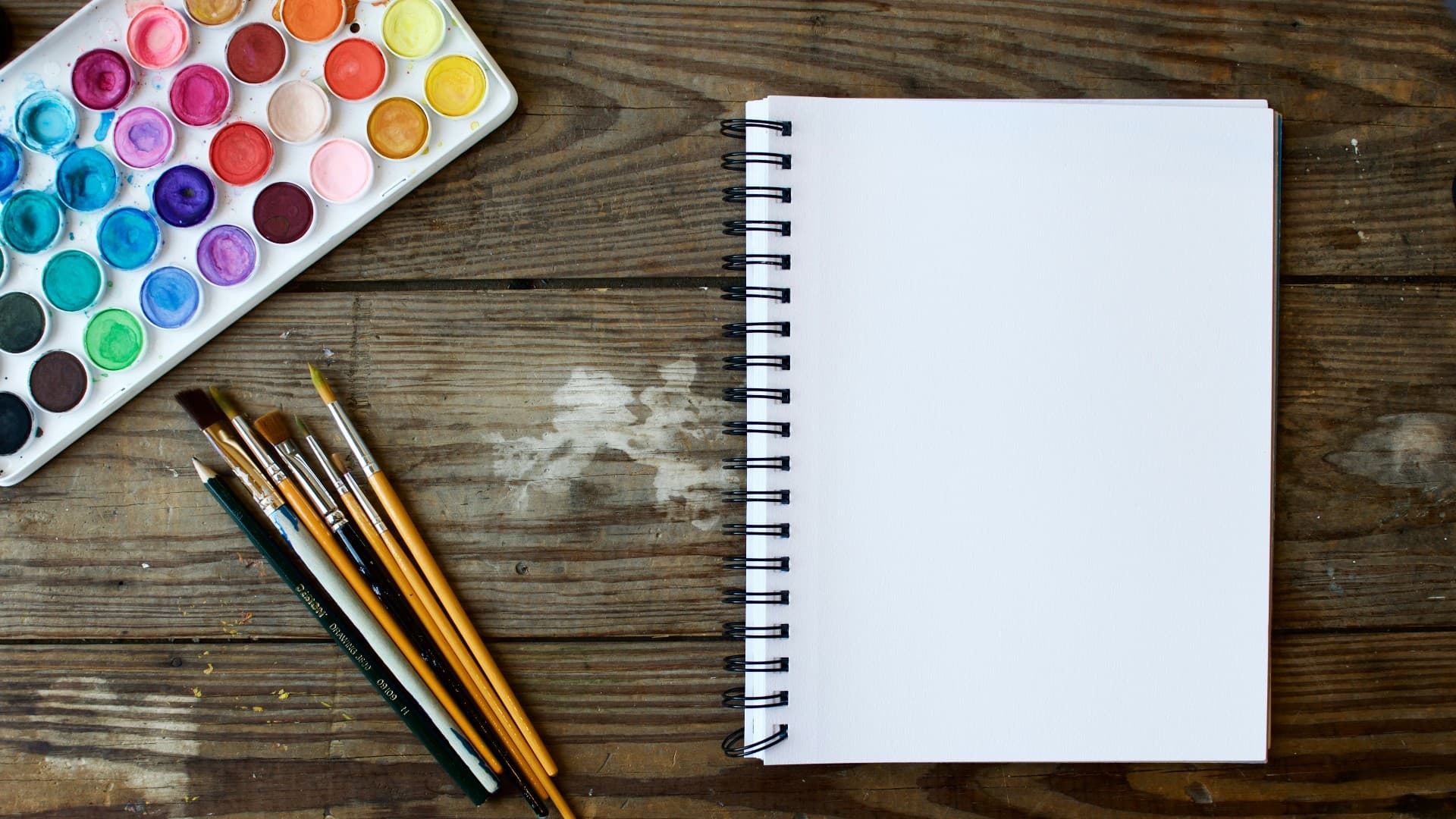 A generic image of watercolours, paint brushes and a notepad on a wooden table. Photo: Unsplash