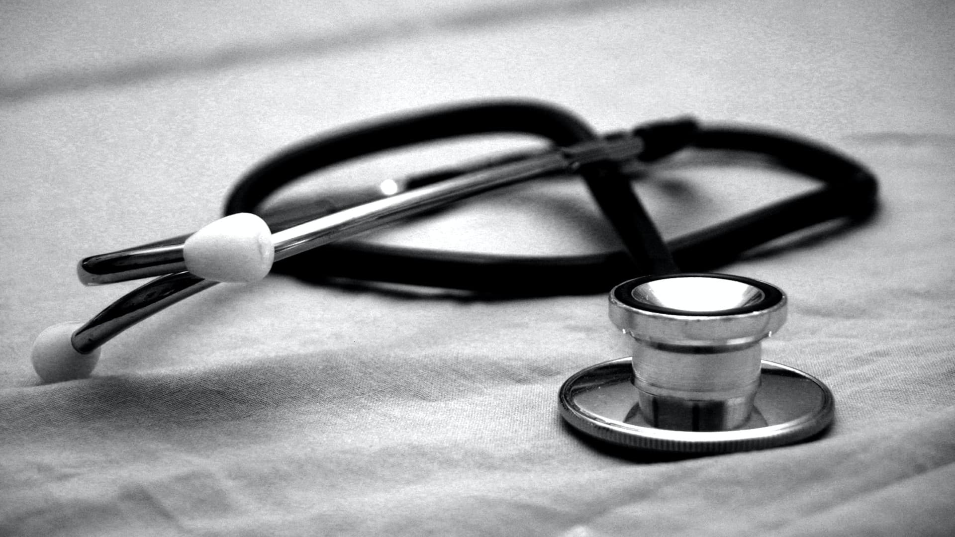A black and white image of a stethoscope on a white hospital bed. Photo: Hush Naidoo Jade, Unsplash