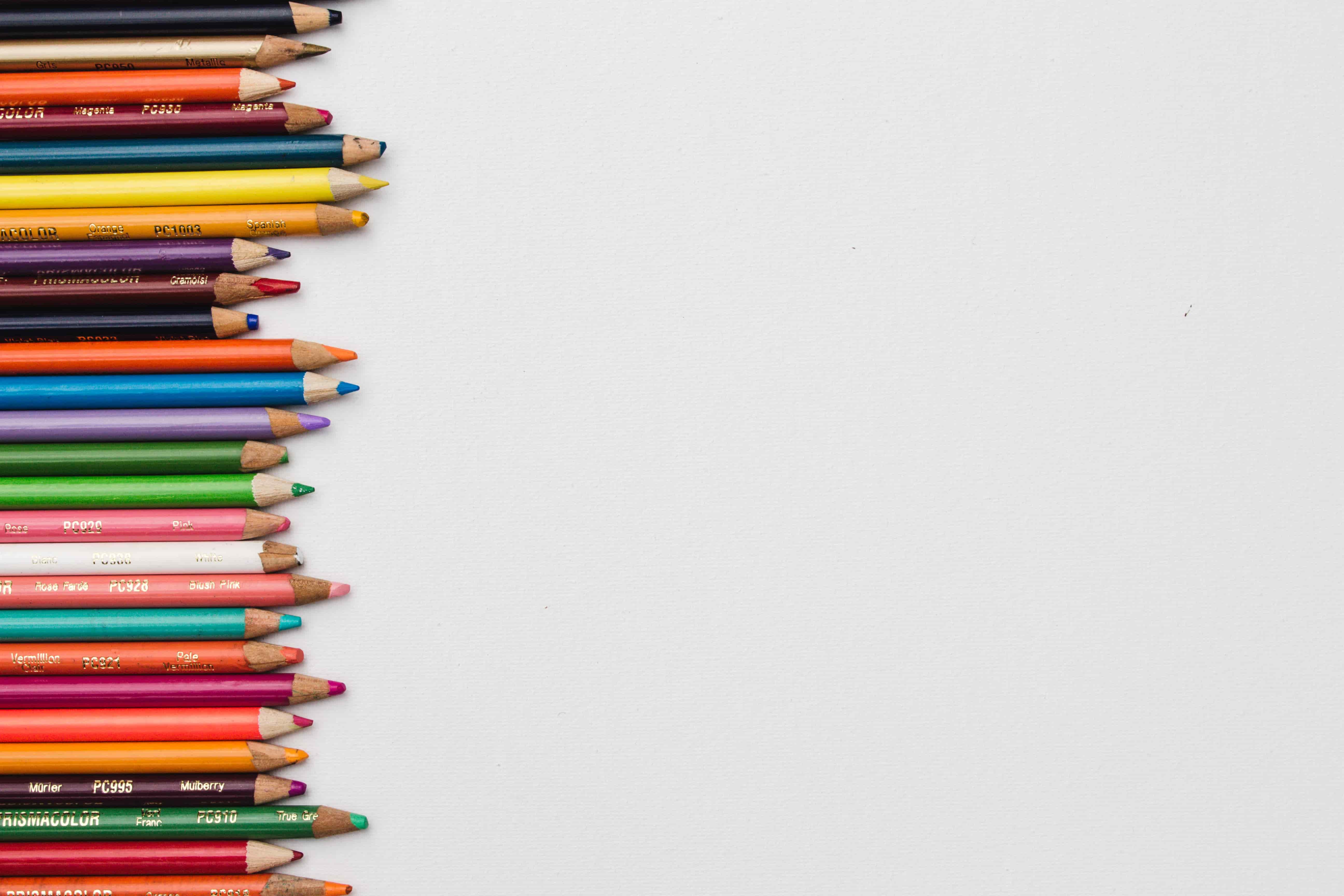 A white background with a selection of coloured pencils along the border on the left-hand side of the image. Photo: Unsplash