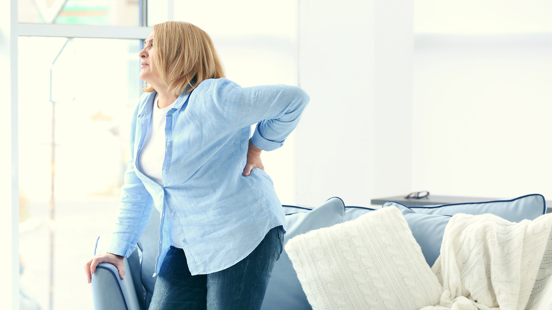 Stock image of a wmen showing chronic back pain. Shuttersock