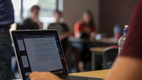 A close up of a laptop with students studying in the background. Photo: UOW