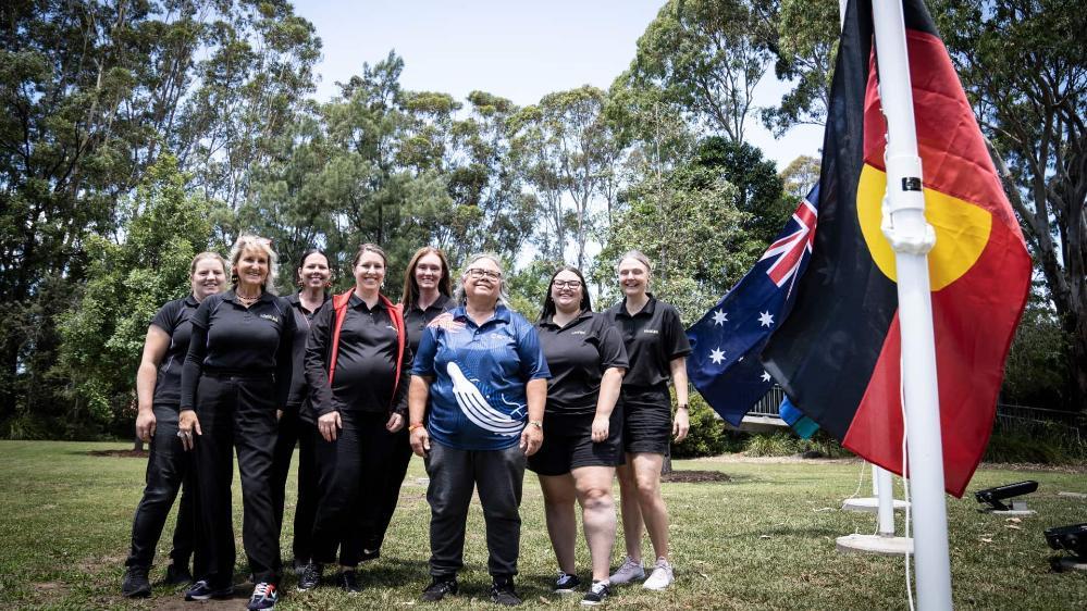 The team from Kids' Uni, with Aunty May, stand alongside the new Aboriginal flag at Wollongong Campus. Photo: Paul Jones