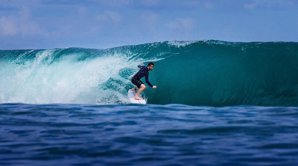 A surfer in a blue rash shirt glides through the waves in Indonesia. Photo: Paul Jones