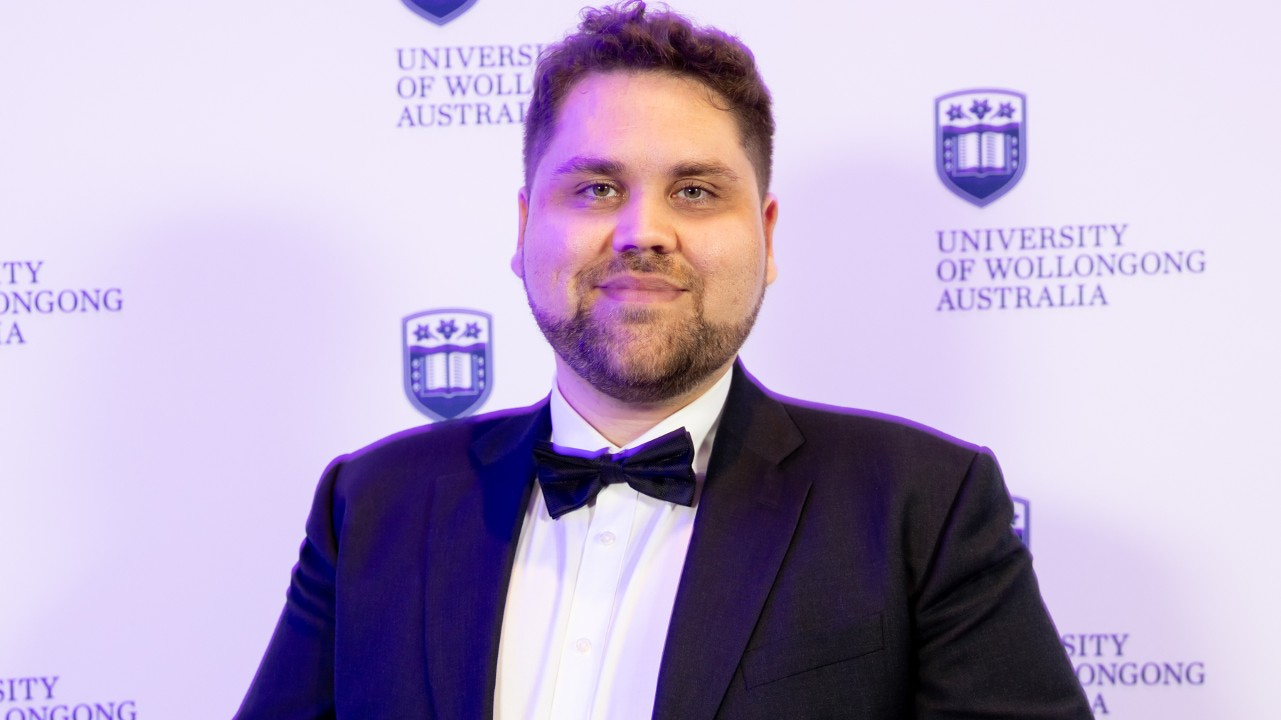 Alumni Award winner Dr Justin Cain holds his award and smiles at the camera. Photo: Mark Newsham