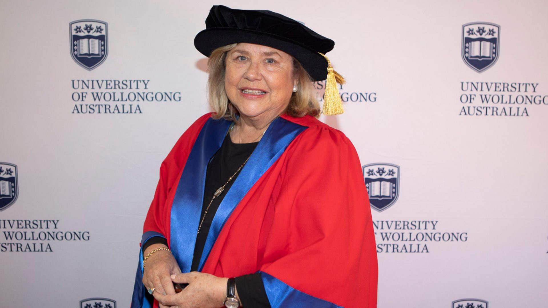 Kim McKay, pictured against a UOW wall, wearing her graduation gown and cap. Photo: Mark Newsham