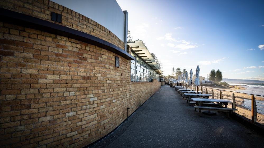 The front of the North Wollongong Bathers Paviliion looks out on to North Wollongong Beach. There is a courtyard with no people and tables and chairs. Photo: Paul Jones