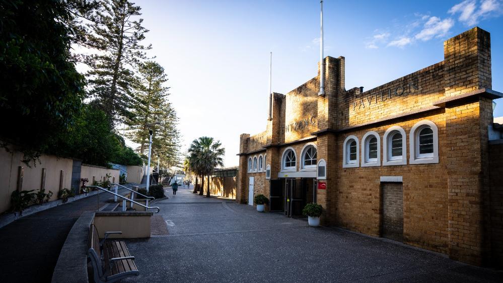 The external left hand side of the North Wollongong Bathers Pavilion. There are trees on the left hand side and an empty courtyard. Photo: Paul Jones