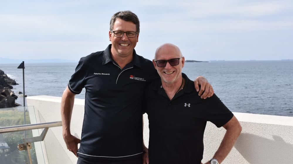 Dr Nathan Knott and Professor Andy stand shoulder to shoulder on a boat, with the ocean in the background. They both wear navy shirts with smiles on their face. Photo: Supplied