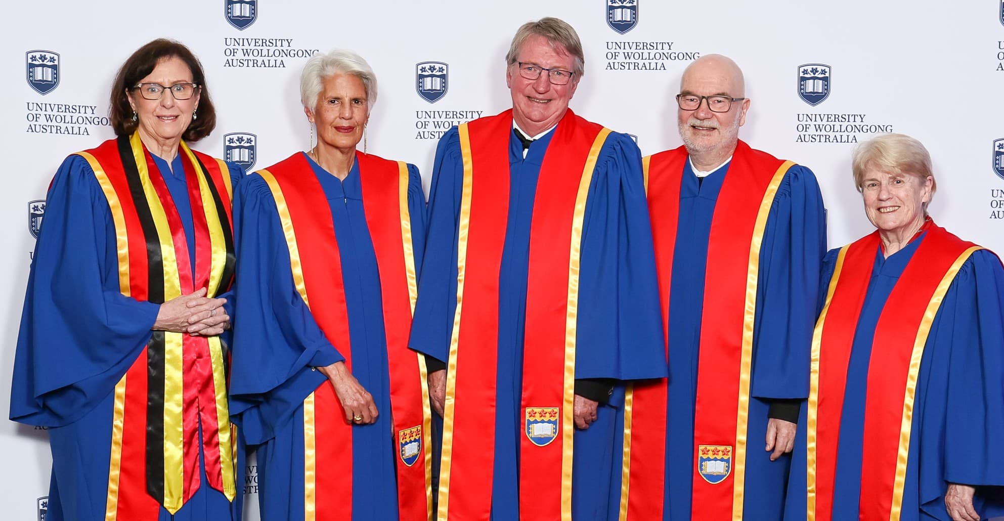 From left, Dr Christine Gillies, Dr Elizabeth Magassy, Mr Barry Irvin, Associate Professor Rodney Vickers and Ms Rosalie Montagner. All are smiling at the camera and wearing the bright red and blue UOW robes. Photo: Denis Ivaneza