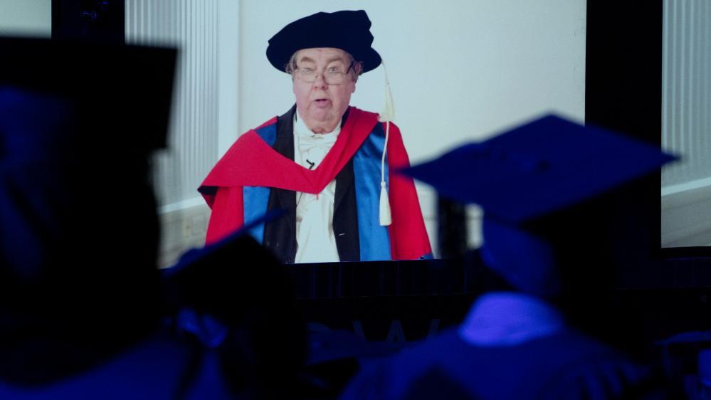 Professor Robin Thompson, pictured on a video screen in a graduation gown and cap, speaks to the audience at the UOW graduation ceremony. Photo: Paul Jones