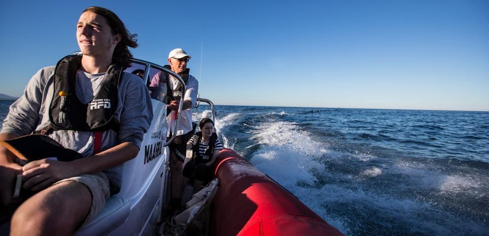 Professor Andy Davis drives a boat in 2015, with two of his marine biology students. Andy is at the helm of the boat, with the ocean in the background. Photo: Paul Jones