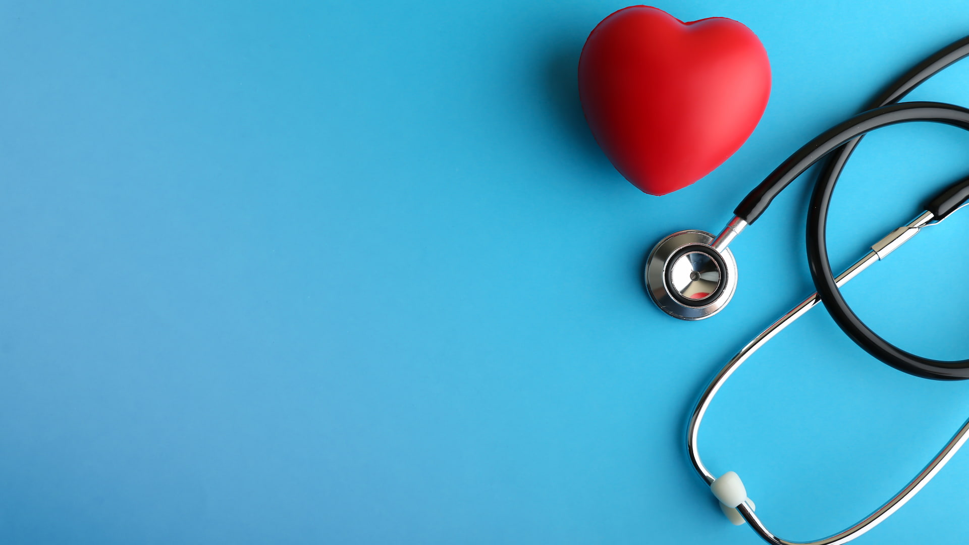 A bright red plastic heart with a stethoscope on a light blue background. Photo: iStock